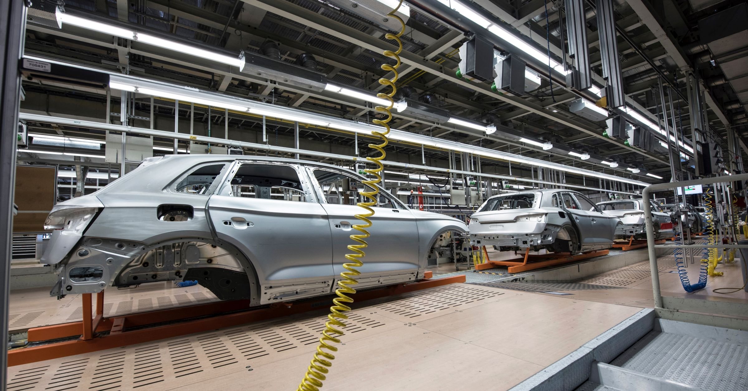 Silver cars being produced in an assembly line in a manufacturing facility.